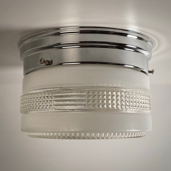 A clean side view of an unlit antique frosted glass flush mount fixture with a polished chrome base and horizontal textured band.