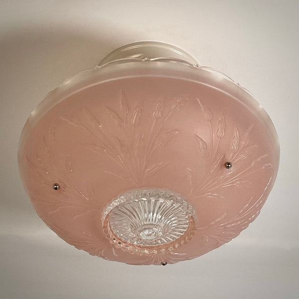 Underside perspective of a pink frosted glass light fixture with molded floral motifs and decorative mounting screws.