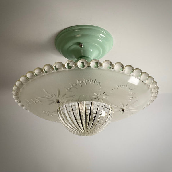 Vintage ceiling light fixture featuring a pastel green metal base and a patterned clear glass shade.