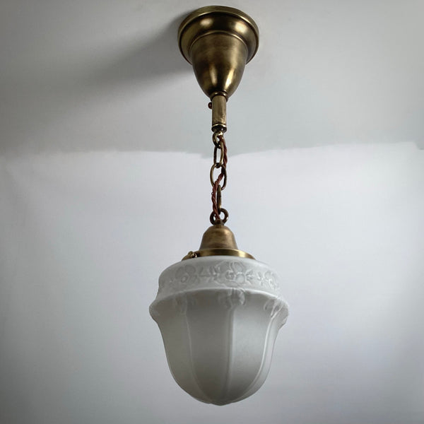 Classic brass hanging ceiling light fixture featuring white embossed frosted glass shade against white background.