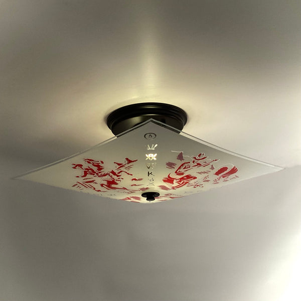 Square vintage frosted glass ceiling light fixture mounted to the ceiling, adorned with red Western prints of cowboys and covered wagons.