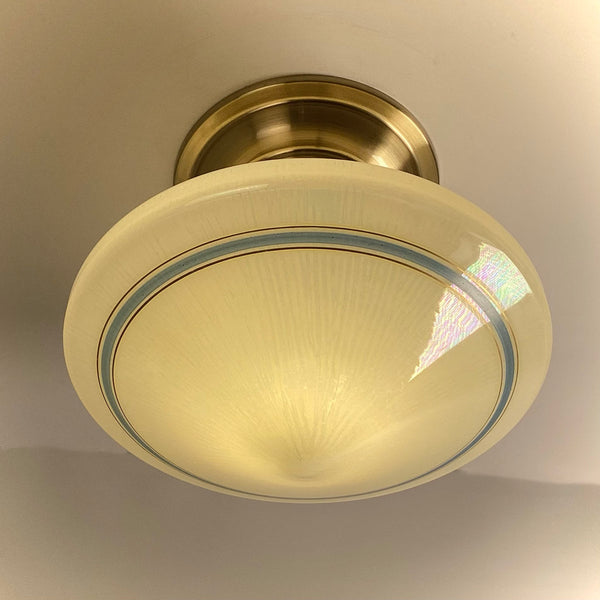 Looking up at a lit Art Deco glass shade, highlighting its original manufactured iridescent sheen and faint gold pinstripes.