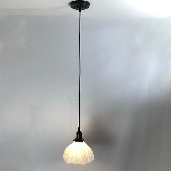 Full view of a black cord pendant light with a lit scalloped milk glass shade.