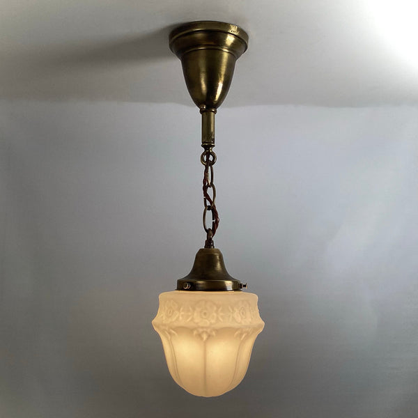 Brass chain pendant light fixture lit with warm ambient light showing floral glass details.