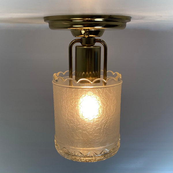 Side angle of a lit brass semi-flush ceiling fixture showing the internal brass socket and textured glass shade.