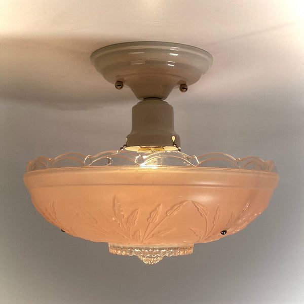 Side view of an illuminated semi-flush mount pink glass ceiling light attached to a white porcelain canopy base.