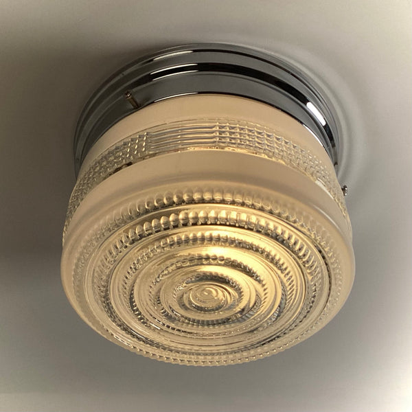 Looking up at an illuminated Art Deco glass ceiling shade, highlighting the bright, glowing concentric circles and textured concentric patterns.