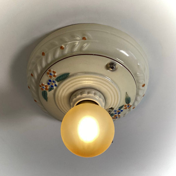 Looking up at the underside of a vintage Art Deco ceramic ceiling light fixture with a pull chain switch and an illuminated bulb.
