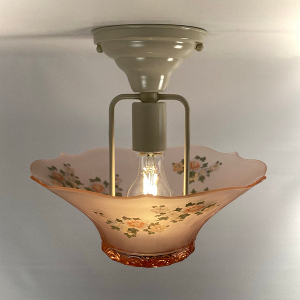 Internal view of the flush mount canopy, bulb socket, and lit lightbulb inside the pink glass fixture.