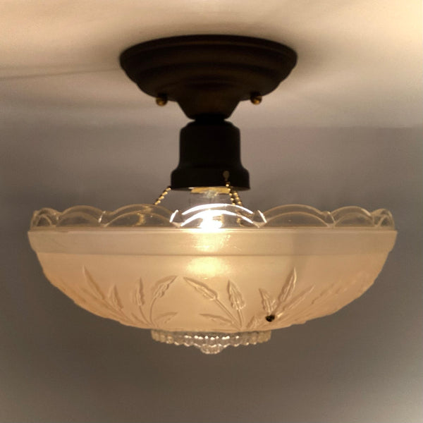 view of a lit vintage semi-flush mount light fixture with a scalloped rim glass shade hanging from chain hardware.