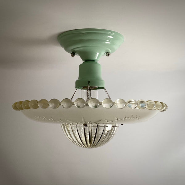 Profile shot of an unlit antique glass ceiling light shade attached to a mint green flush mount.