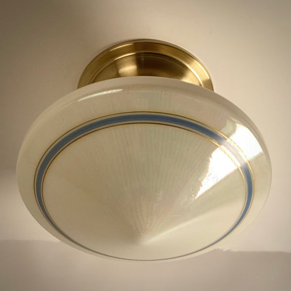 Bottom view of the unlit cone-shaped vintage opal glass shade showing the concentric blue band design and modern brass base.