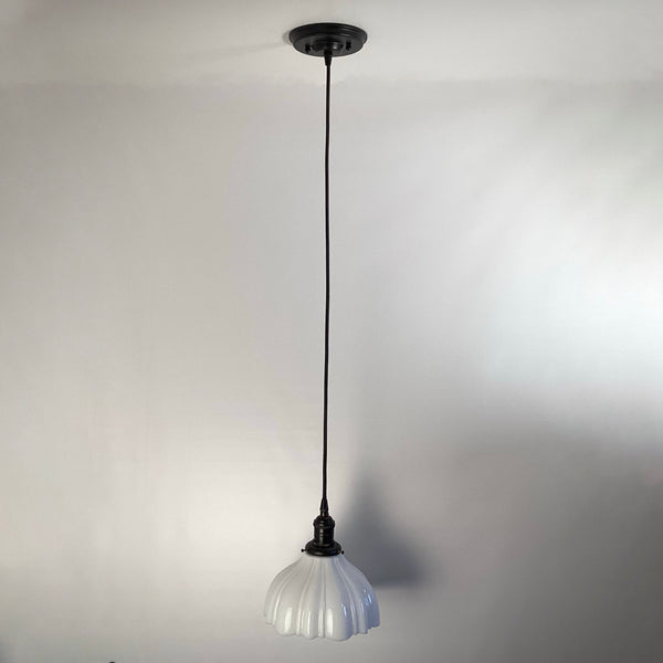 Full length view of a minimalist black cord pendant light with white scalloped shade.