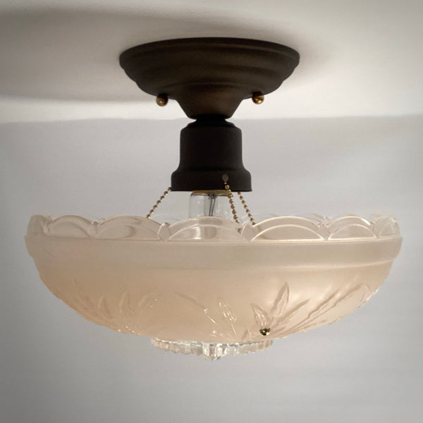 Side profile of a vintage semi-flush ceiling light with a dark bronze base, ball chain supports, and scalloped frosted glass bowl.