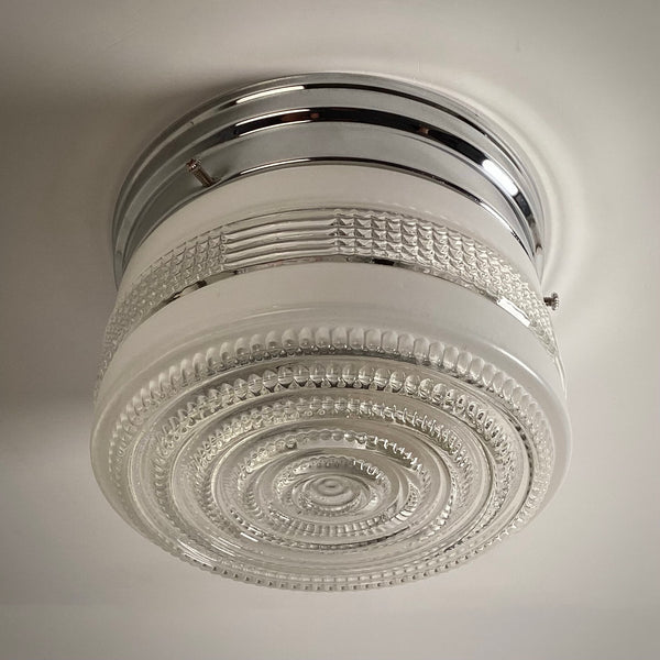 A bottom-up view of a vintage concentric circle glass light fixture, turned off, showing the clear detail of the ribbed and beaded glass design.