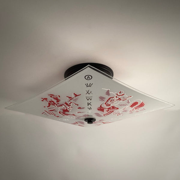 Square vintage frosted glass ceiling light fixture mounted to the ceiling, adorned with red Western prints of cowboys and covered wagons.