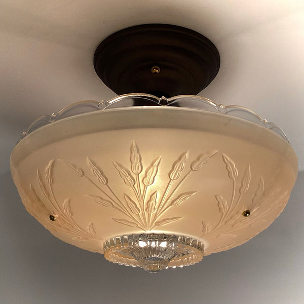 Warmly lit close-up of an antique-style frosted glass shade featuring embossed plant stems and dark ceiling canopy.