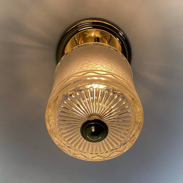 Bottom-up view of a lit vintage ceiling fixture highlighting the sunburst cut glass design and brass centerpiece.