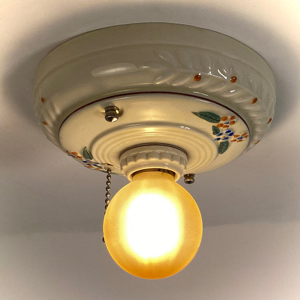 A classic porcelain pull chain ceiling light fixture turned on, casting a soft amber glow in a white room.