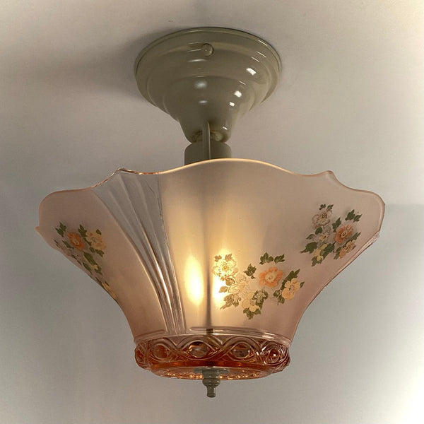 Side profile of an illuminated pink glass ceiling fixture with wild rose floral pattern and molded glass rim.