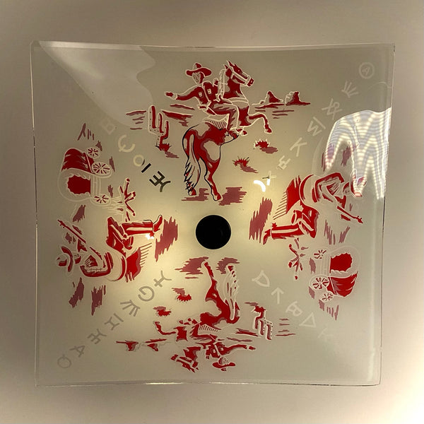 Direct overhead view of a square glass light shade with red Western illustrations of cowboys, campfire scenes, and cattle brands around a center hole.
