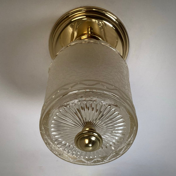 Low-angle shot looking up at an unlit glass cylinder light fixture with a radial cut-glass base and polished brass finial.