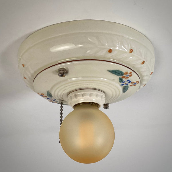 A close-up macro view of the hand-painted blue and orange floral pattern on a vintage ceramic ceiling light fixture glaze.