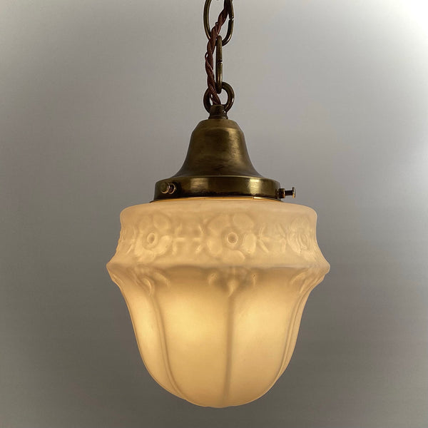 Detail view of frosted glass pendant light shade showing embossed pattern and brass chain mount.