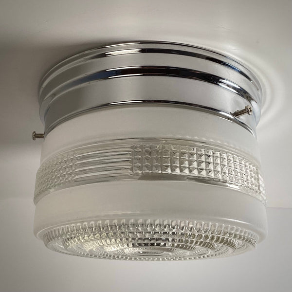 An angled side profile of an unlit mid-century drum ceiling light fixture with visible mounting screws on the chrome base.
