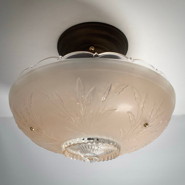 Perspective view of a vintage frosted glass ceiling fixture showing subtle raised relief leaves and dark mounting hardware.