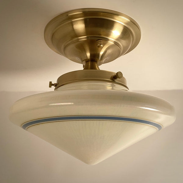 Side view of a restored antique schoolhouse light fixture with a smooth cream-colored glass shade and single blue accent line.