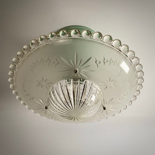 Bottom view of an unlit vintage ceiling light shade showing clear beaded trim and starburst engravings.
