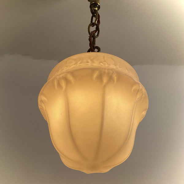 Close-up angled view of illuminated frosted glass pendant shade highlighting fluted and floral design.