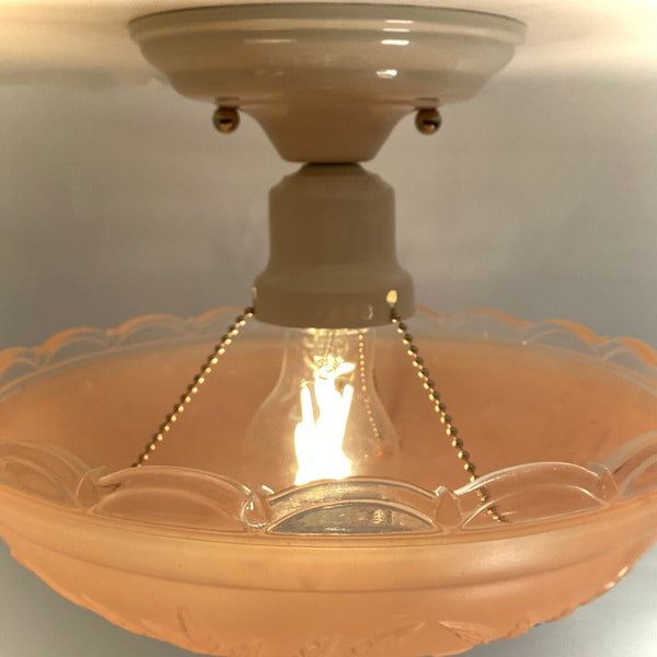 Close-up of the interior lit light bulb and three-chain support hardware inside a pink frosted glass shade.