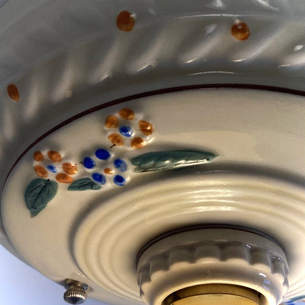 A detailed macro shot showing the metallic pull chain mechanism and painted flower details on a 1930s porcelain light fixture.