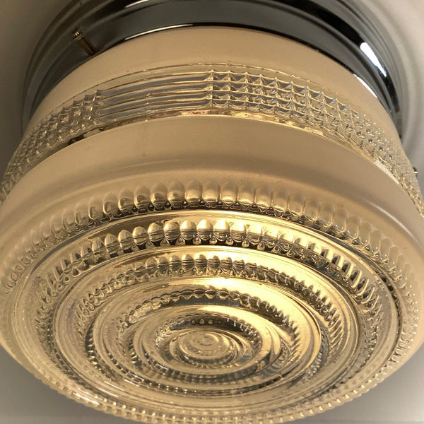 A dramatic, extreme close-up view looking up at the illuminated textured glass of an Art Deco ceiling light, showing detailed patterns and warm light refraction.