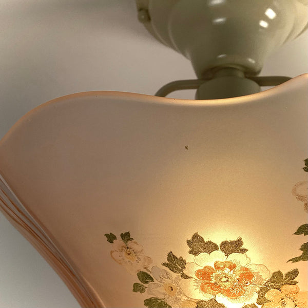 Extreme close-up of a tiny dark spot flaw on the pink frosted glass shade near the floral print.