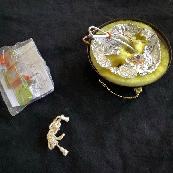 The reverse side of a bronze ceiling light fixture canopy displaying the electrical wiring, foil backing, and yellow fiberglass insulation, alongside its mounting hardware kit.