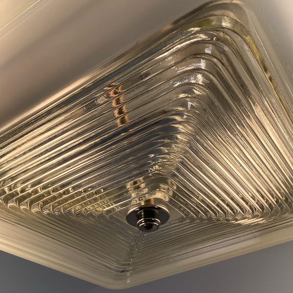 Angled close-up of mid-century square ceiling light with aluminum fixture base and stepped glass shade, illuminated detail — Vintporium
