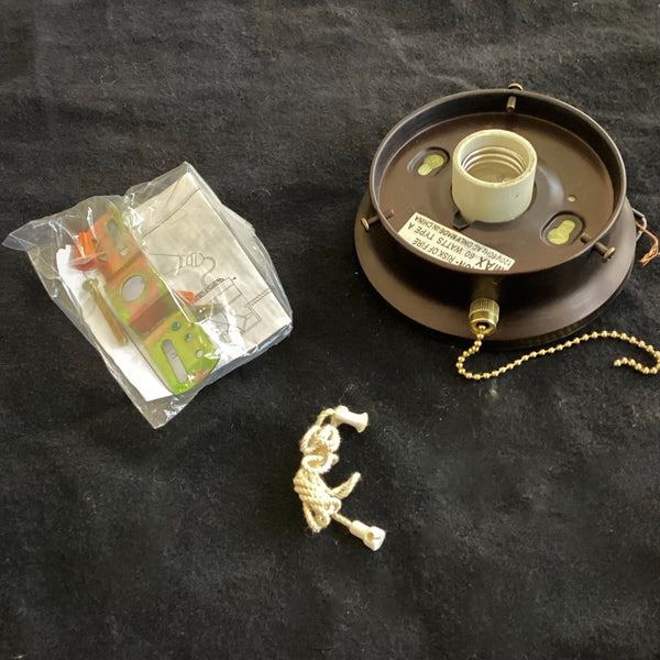Top view of a dark bronze ceiling light fixture base with a ceramic bulb socket and a gold pull chain, shown next to an installation hardware pack and extension string on a black background.