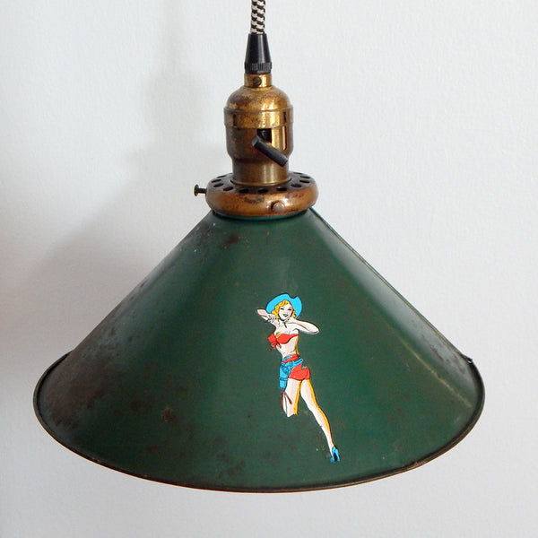 Originally made for the Vintporium workshop, this distressed and worn green metal swag light has been updated with a new houndstooth fabric cord with molded plug. new turn-key socket guts, socket cardboard insulation, metal cord grip, and vintage distressed Impko cowgirl pinup decal on the shade. The shade has surface rust, scrapes, and other battle scars. The socket has wear and age marks. Available at www.vintporium.com